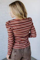 Person wearing a striped long-sleeve shirt against a white wall