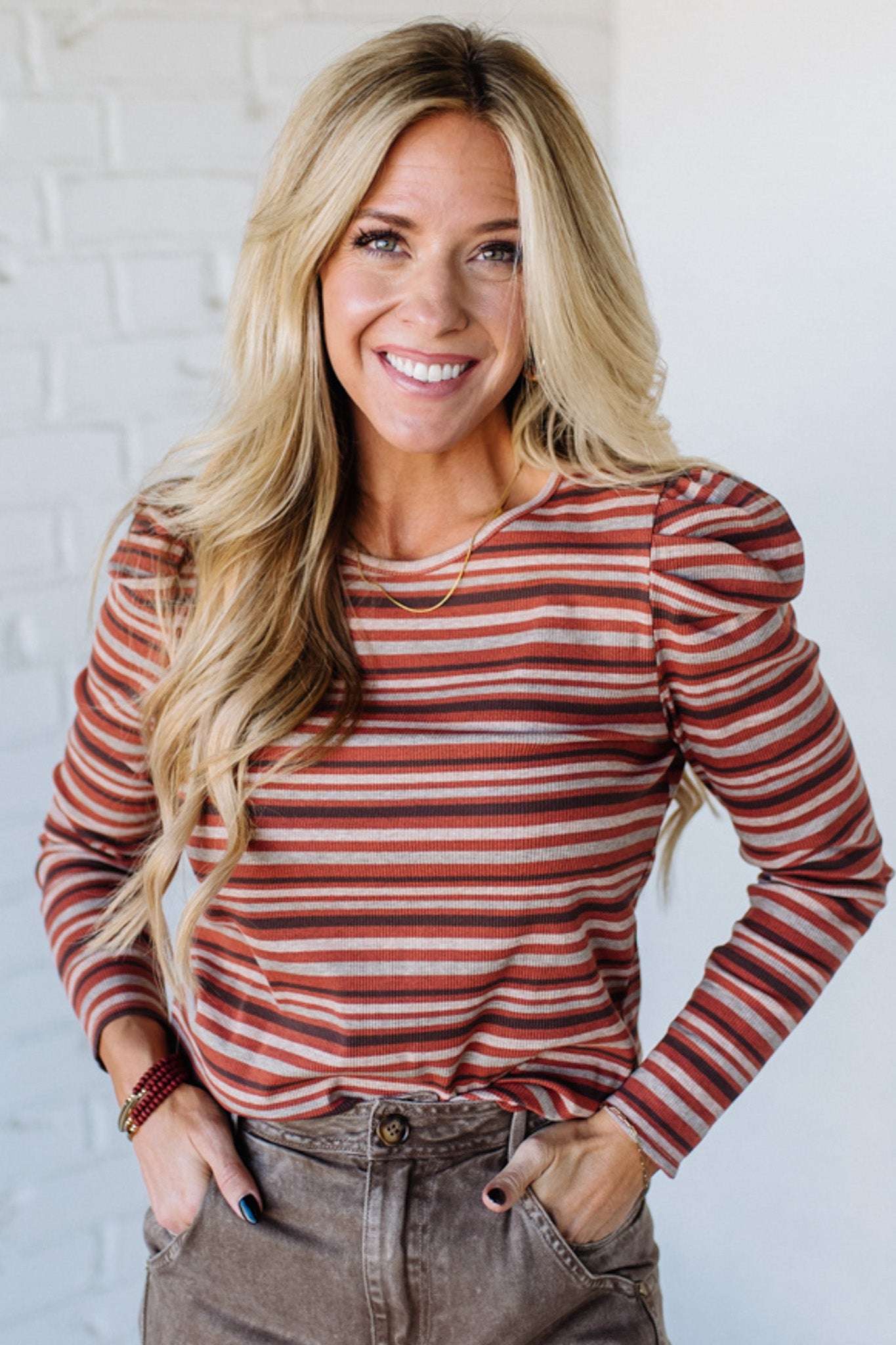 Woman wearing a red and white striped long-sleeve top against a white brick wall.