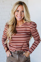 Woman wearing a red and white striped long-sleeve top against a white brick wall.