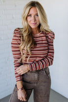 Woman wearing a striped sweater and brown pants against a white brick wall.