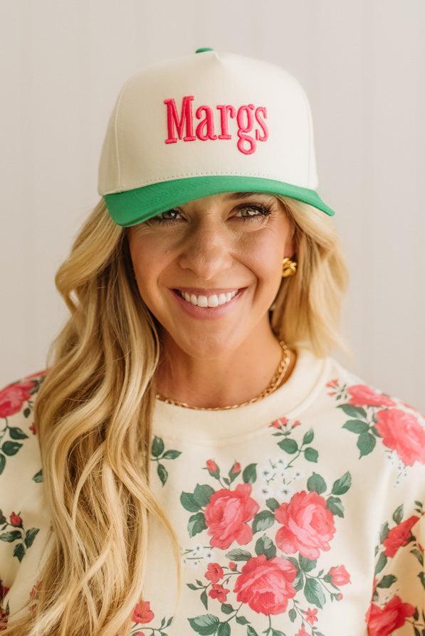 Woman wearing a cap with 'Margs' on it against a plain background