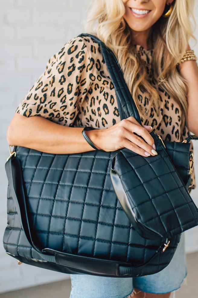 Woman holding a black nylon quilted traveler tote bag.