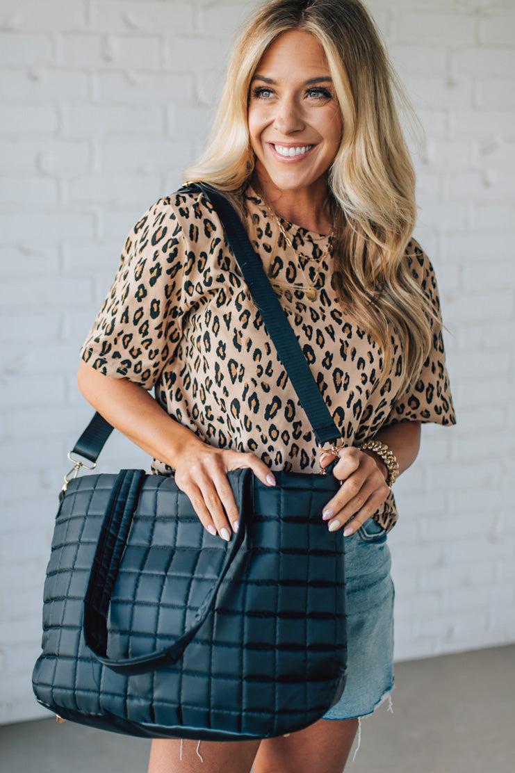 Woman holding a black nylon quilted traveler tote bag.