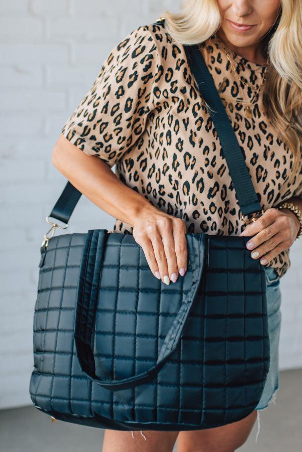 Woman holding a black nylon quilted traveler tote bag.