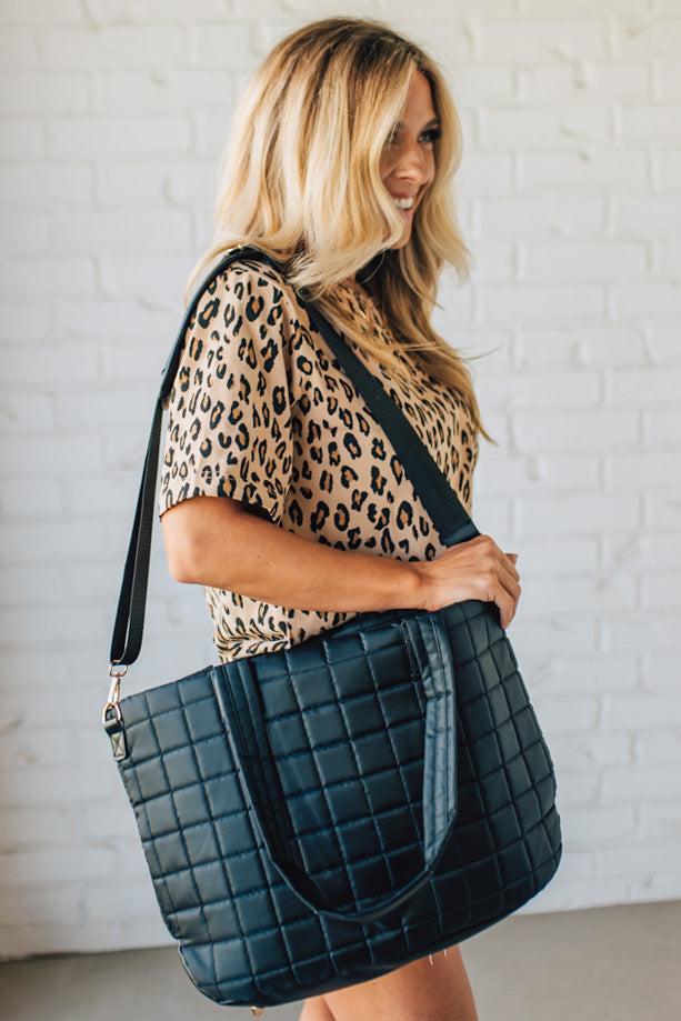 Woman holding a black nylon quilted traveler tote bag.