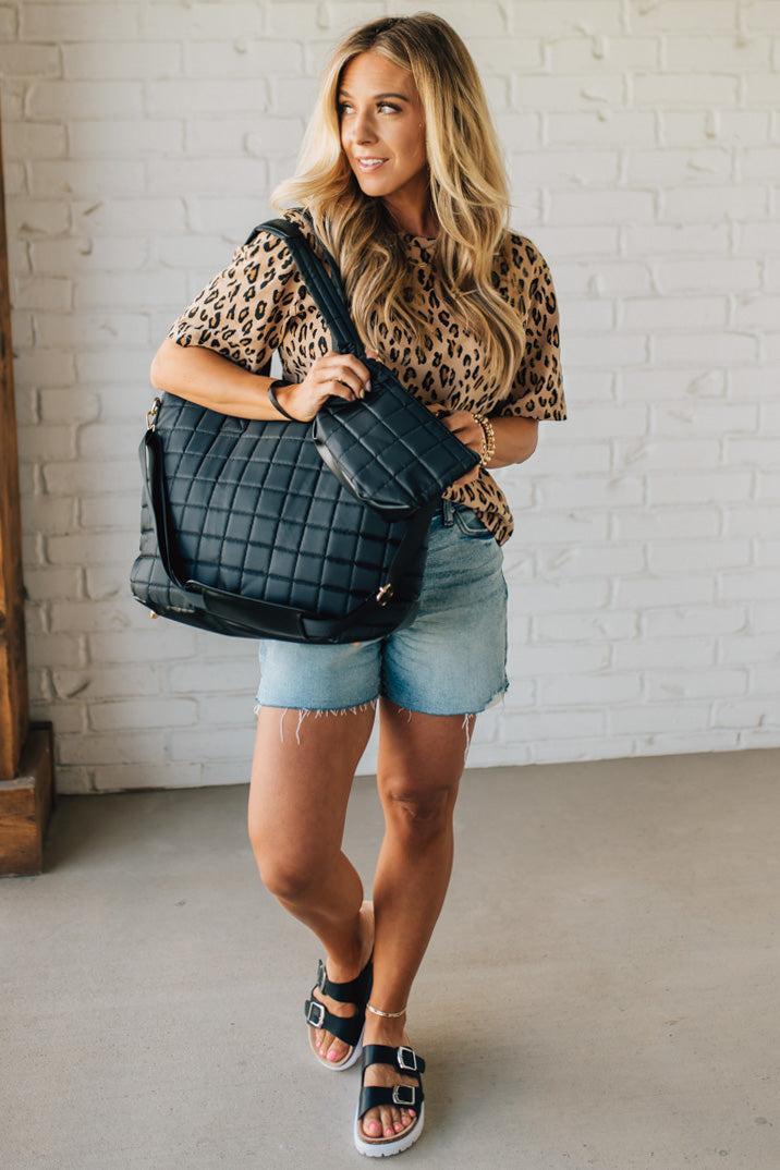 Woman holding a black nylon quilted traveler tote bag.