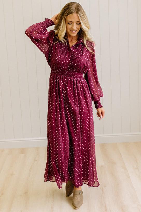 Blonde woman in a brightly lit studio wearing boots and a long dark red dress with full button front and pintucked bodice.