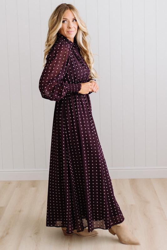 Blonde woman in a brightly lit studio wearing boots and a long dark purpleish brown dress with full button front and pintucked bodice.