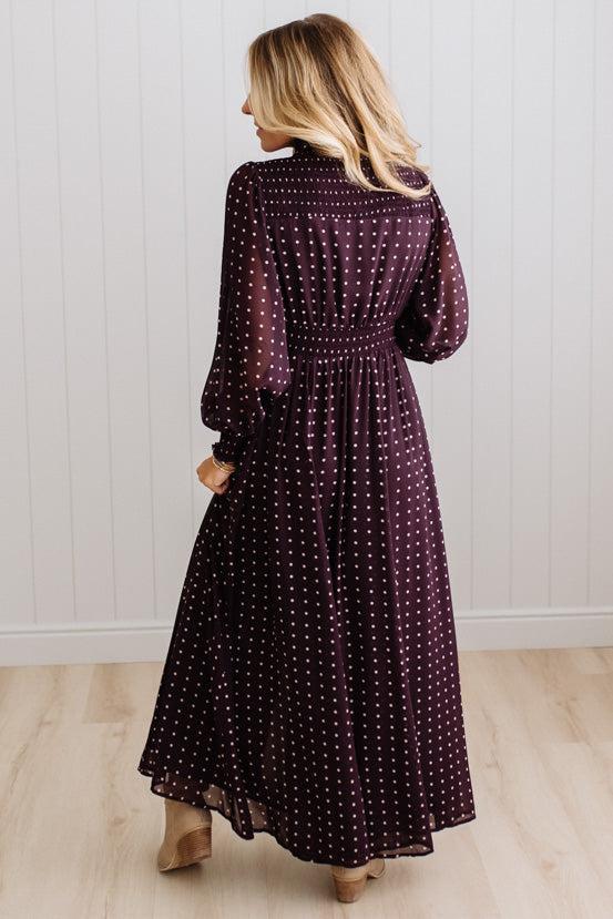 Blonde woman in a brightly lit studio wearing boots and a long dark purpleish brown dress with full button front and pintucked bodice.