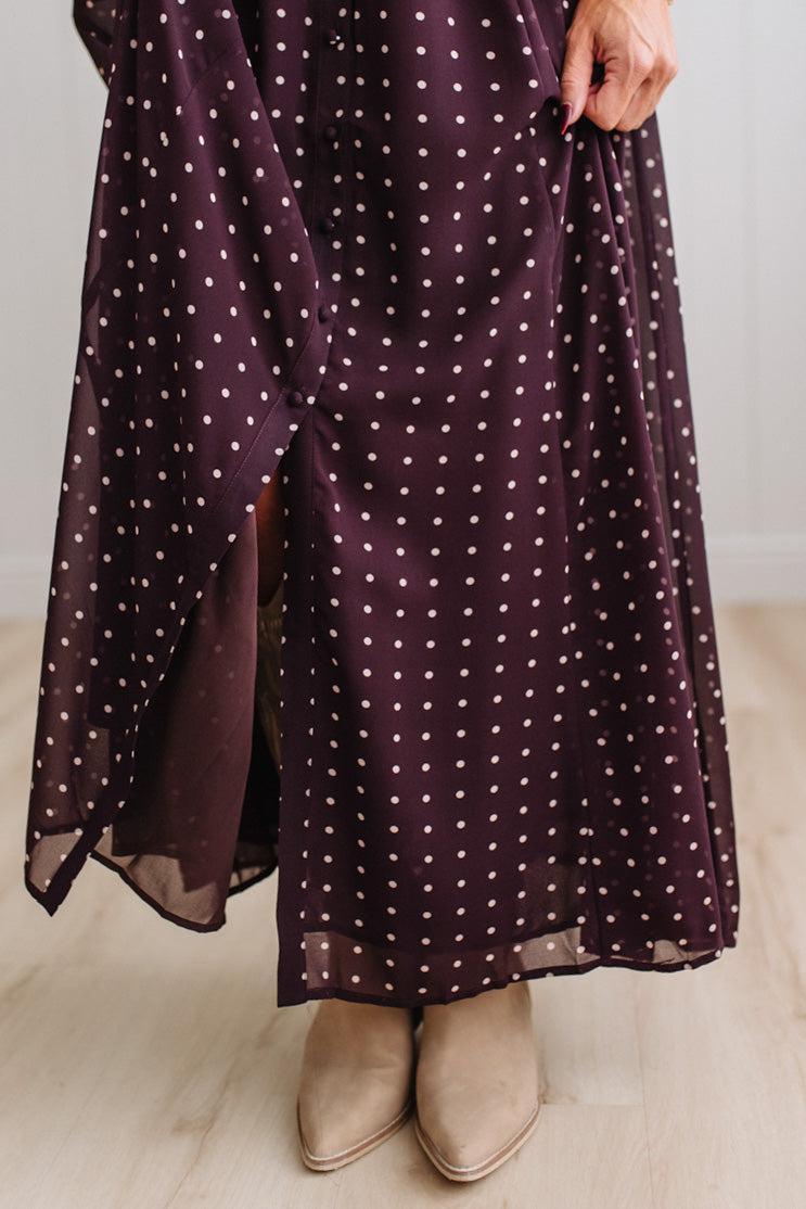 Blonde woman in a brightly lit studio wearing boots and a long dark purpleish brown dress with full button front and pintucked bodice.