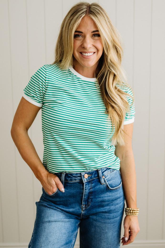 Woman wearing a green and white striped shirt and blue jeans against a neutral background