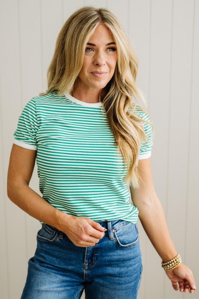 Woman wearing a green and white striped shirt and blue jeans against a light wooden panel background