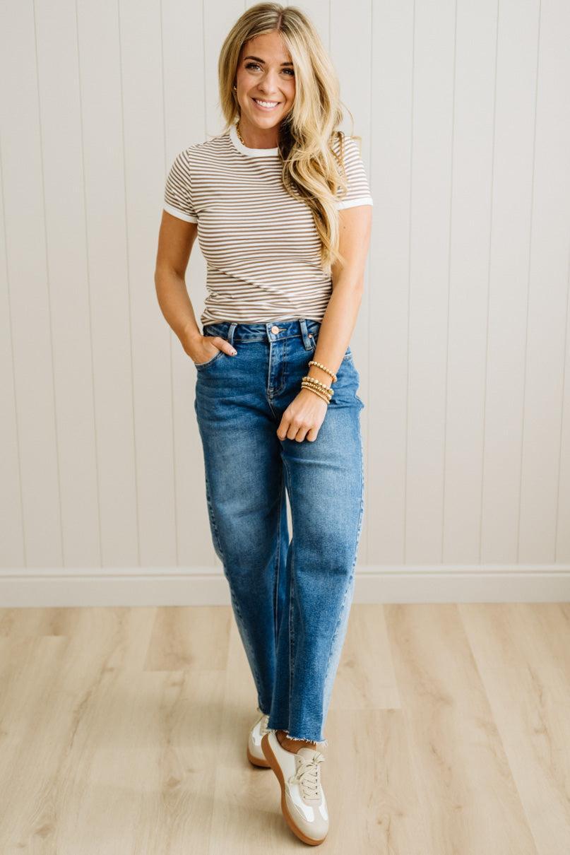 Woman wearing a striped shirt and blue jeans standing against a white wall.