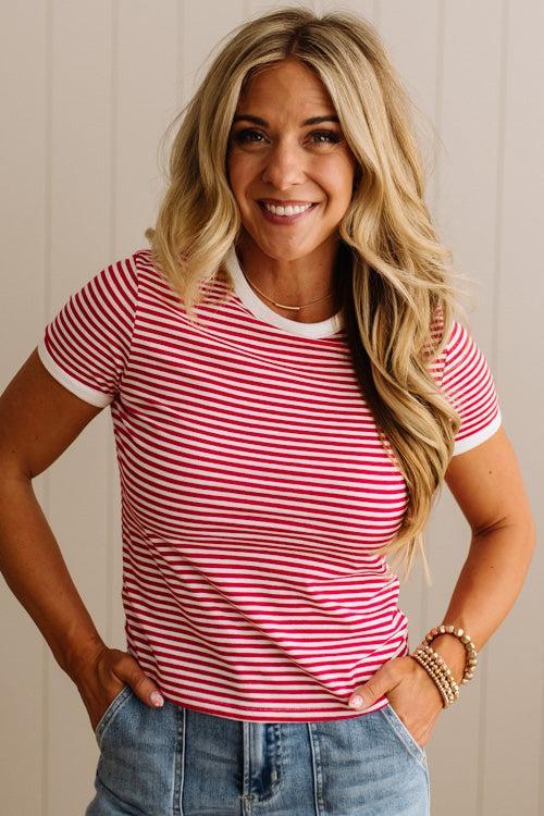 Woman wearing a red and white striped shirt with blue jeans against a neutral background