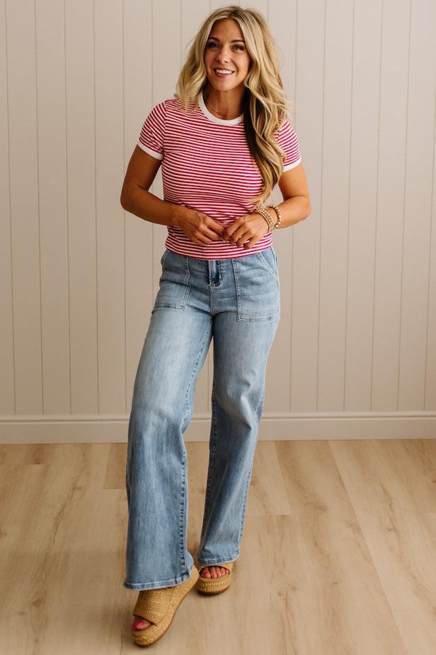 Woman wearing a striped shirt and jeans standing against a beige wall.