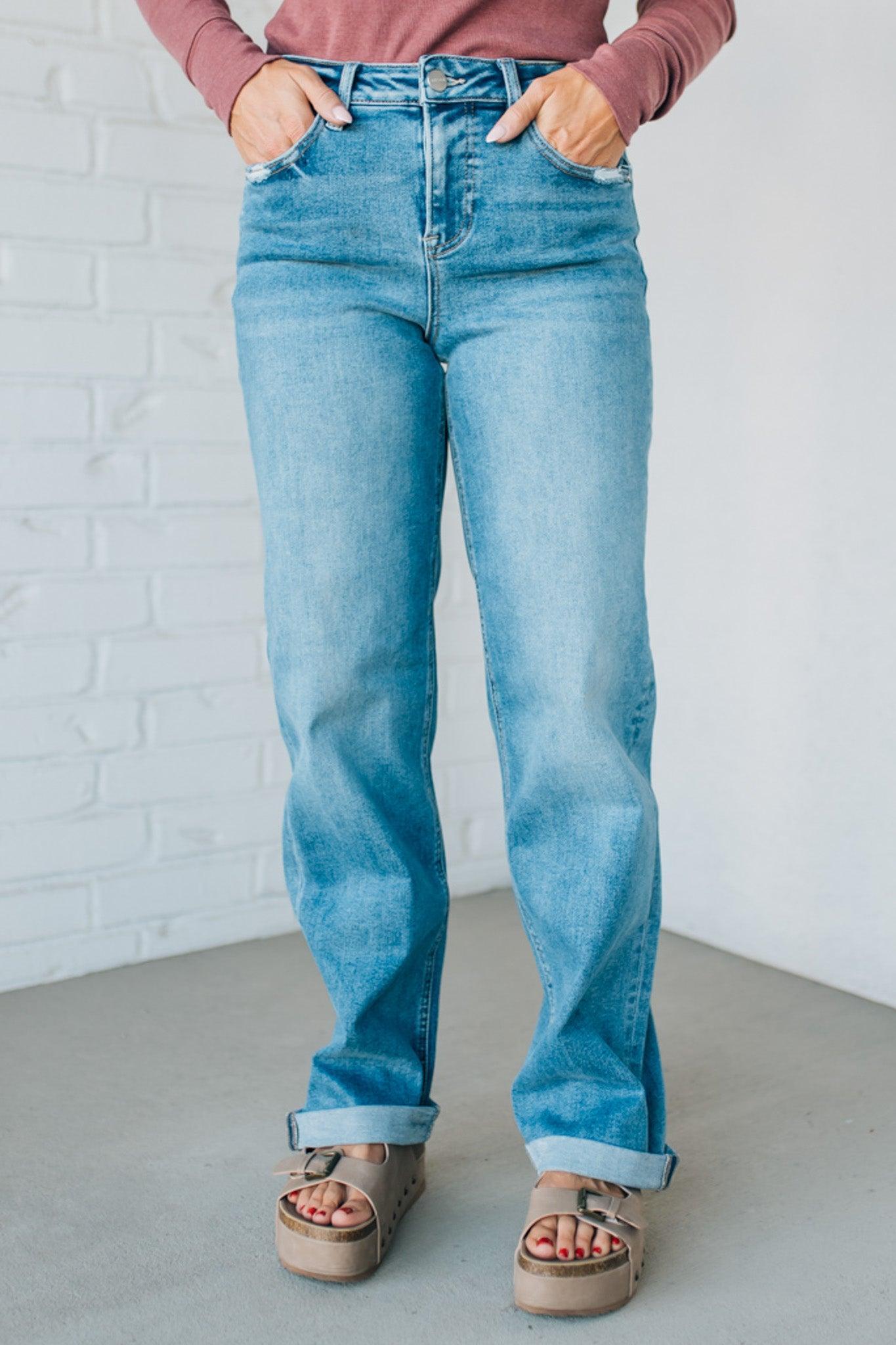 Person wearing blue jeans and a pink top against a white brick wall.