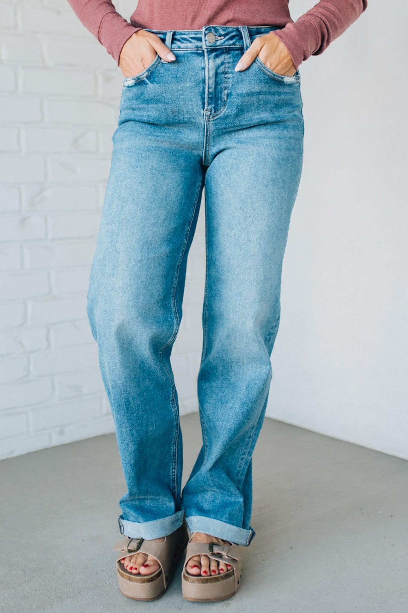 Person wearing blue jeans and a pink top against a white brick wall.