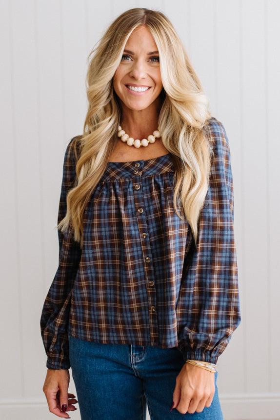 Blonde woman in a brightly lit studio wearing a PLAID SQUARE NECK BUTTON CLOSURE FRONT LONG SLEEVE BLOUSE WITH DARK JEANS AND BROWN BOOTS.