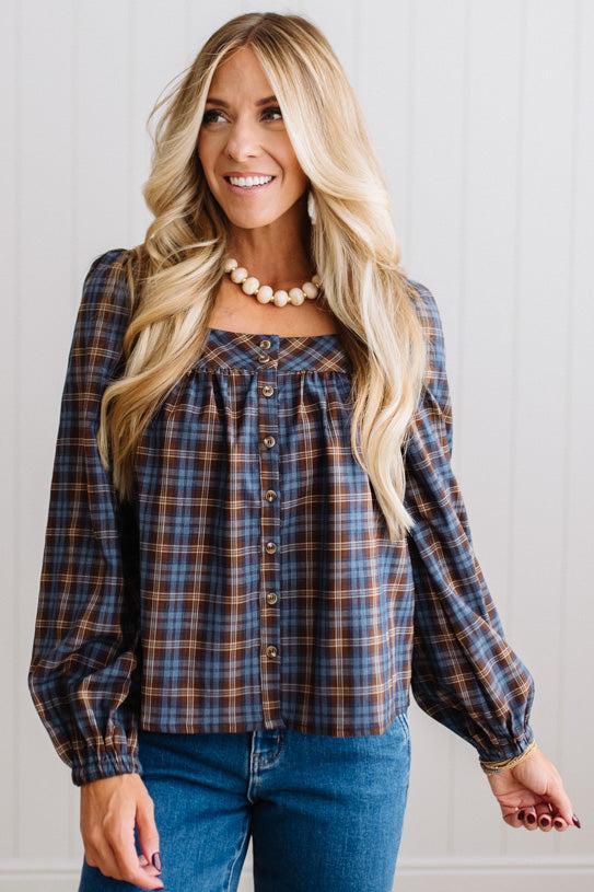 Blonde woman in a brightly lit studio wearing a PLAID SQUARE NECK BUTTON CLOSURE FRONT LONG SLEEVE BLOUSE WITH DARK JEANS AND BROWN BOOTS.