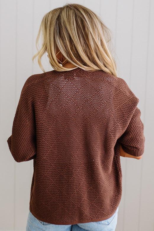 Person wearing a brown textured sweater with a neutral background
