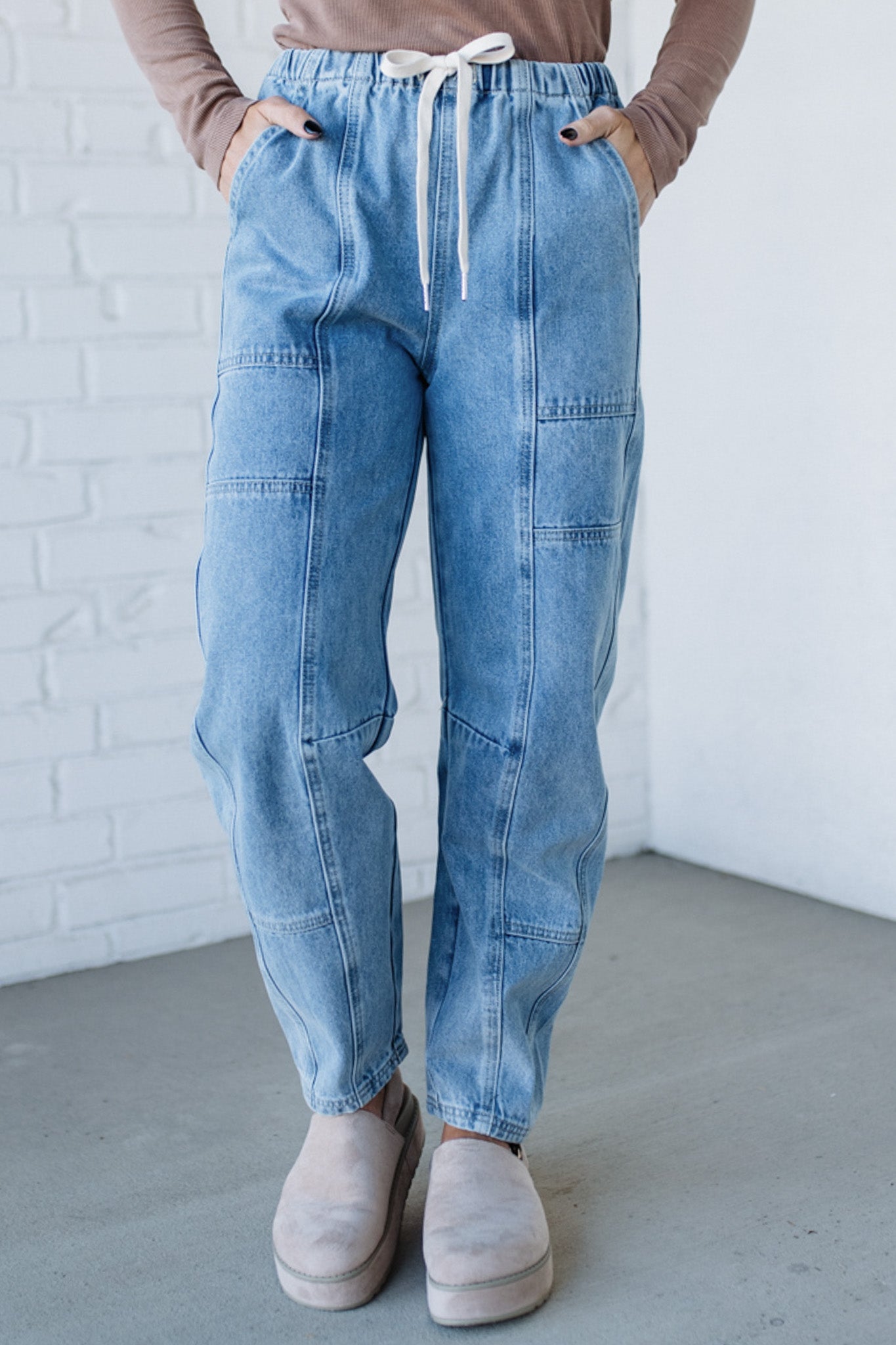 Person wearing light blue denim pants with a white brick wall background