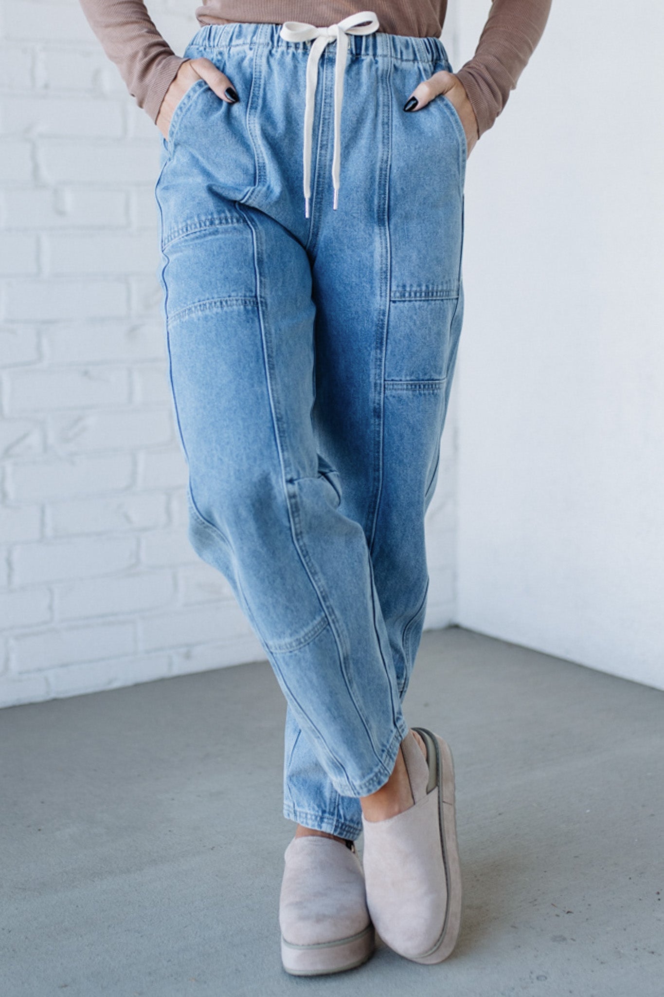 Person wearing blue jeans and beige shoes against a white brick wall.