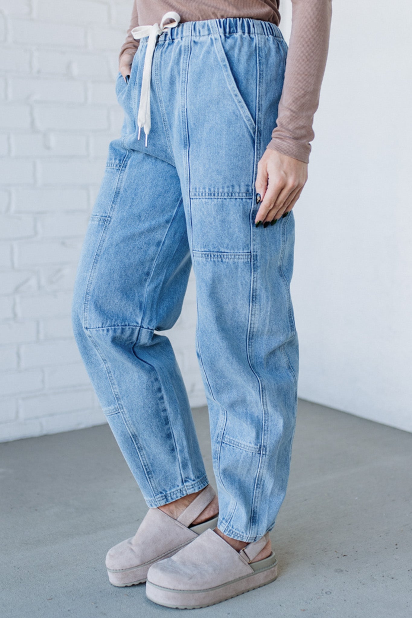 Person wearing light blue jeans and beige shoes against a white brick wall.
