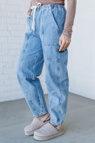 Person wearing light blue jeans and beige shoes against a white brick wall.