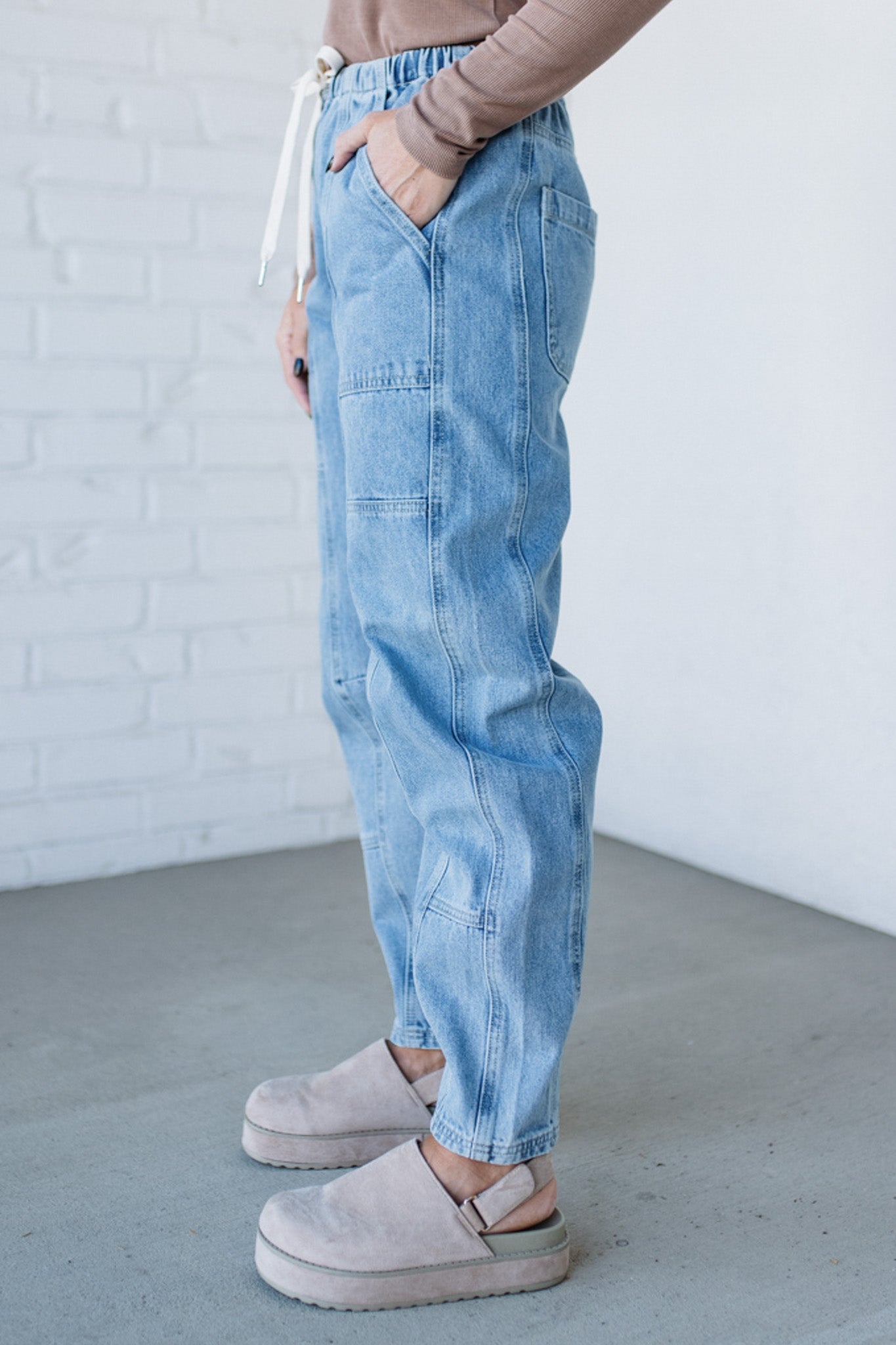 Person wearing light blue jeans and pink shoes against a white brick wall.