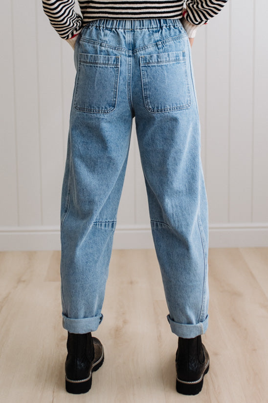 Person wearing light blue denim pants with a paneled wall background