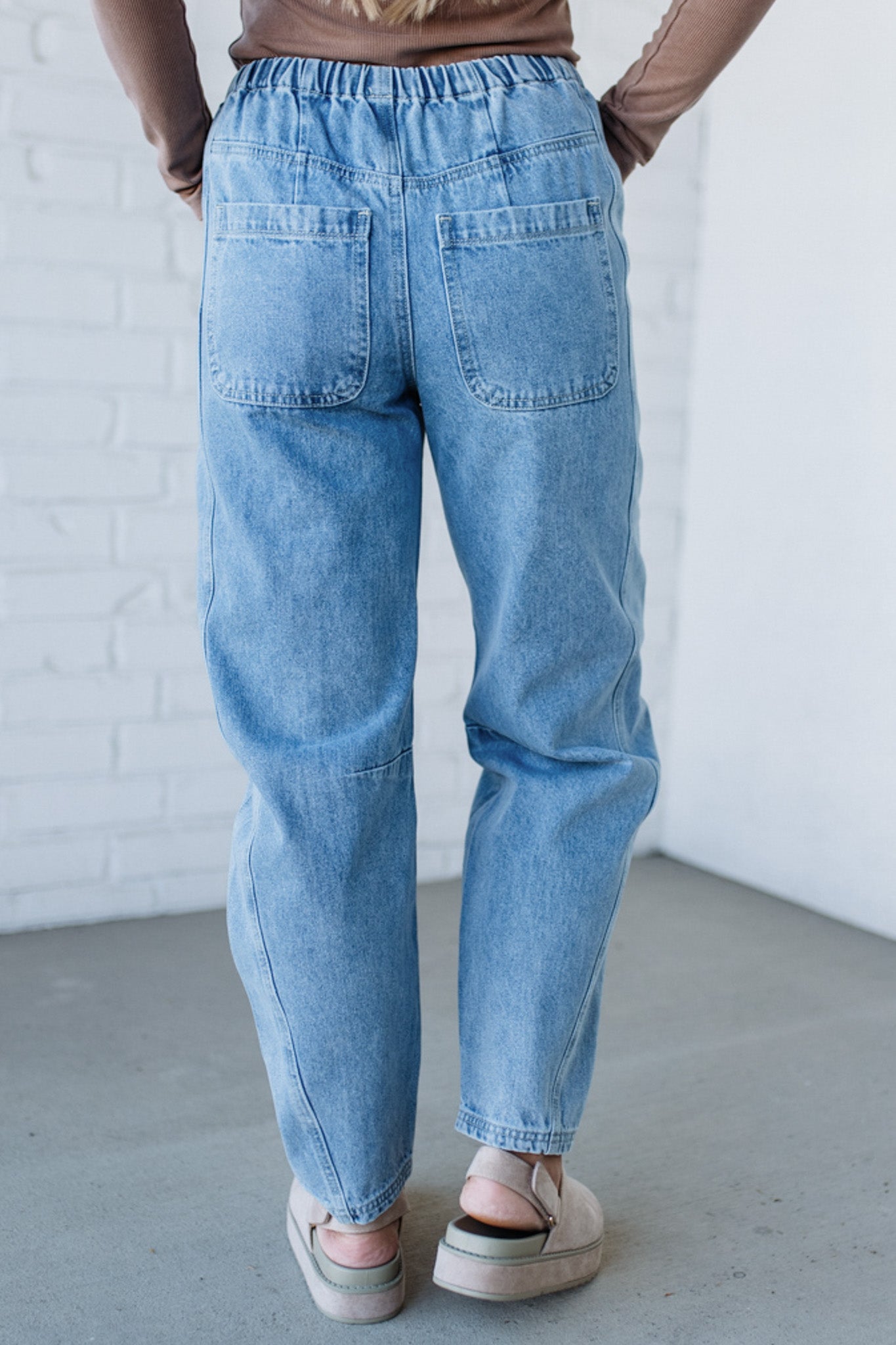 Person wearing light blue jeans against a white brick wall.