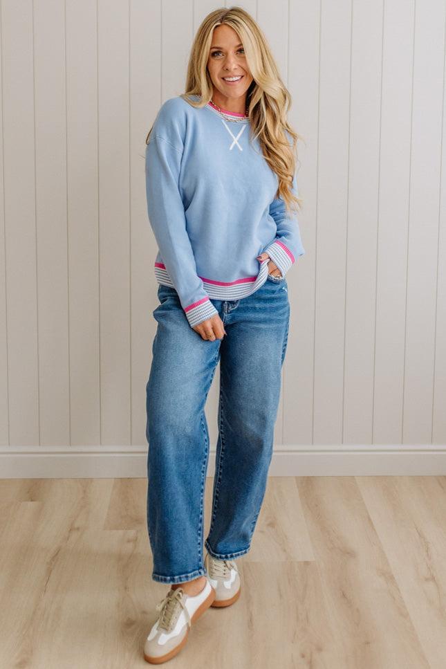 Woman wearing a light blue sweater and jeans standing against a white paneled wall.