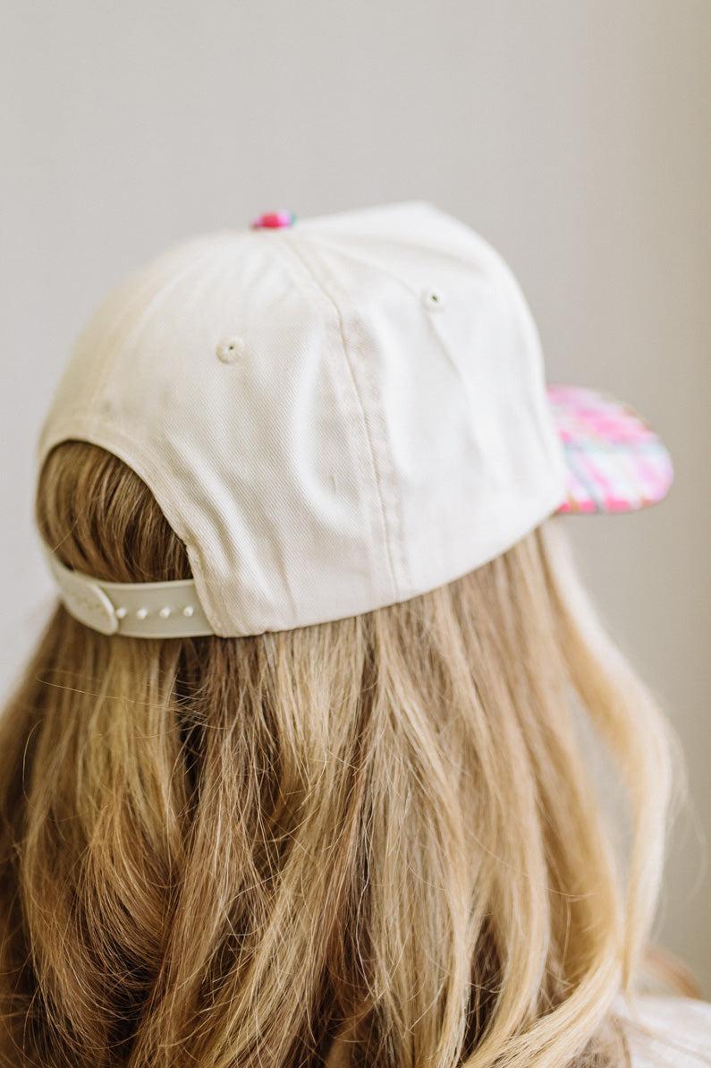 cream trucker cap pairs a crisp structured crown with a playful plaid brim in pink, green, and yellow, topped off with bold "Merry & Bright" embroidery in festive multicolor lettering
