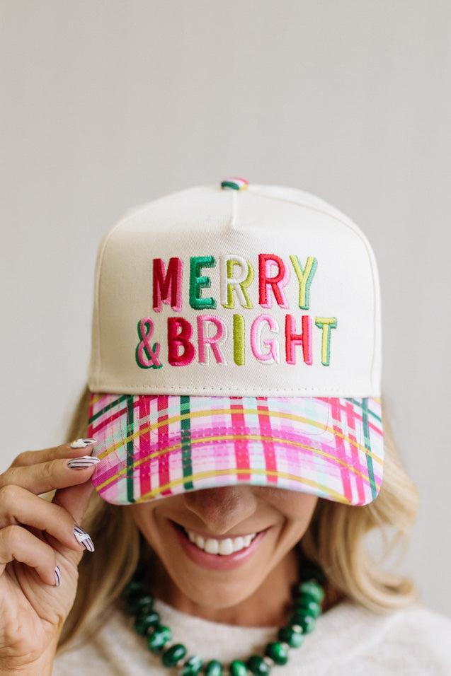 cream trucker cap pairs a crisp structured crown with a playful plaid brim in pink, green, and yellow, topped off with bold "Merry & Bright" embroidery in festive multicolor lettering