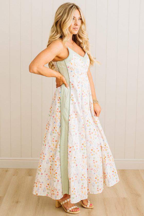 Woman wearing a floral dress with a green side panel against a white wall.