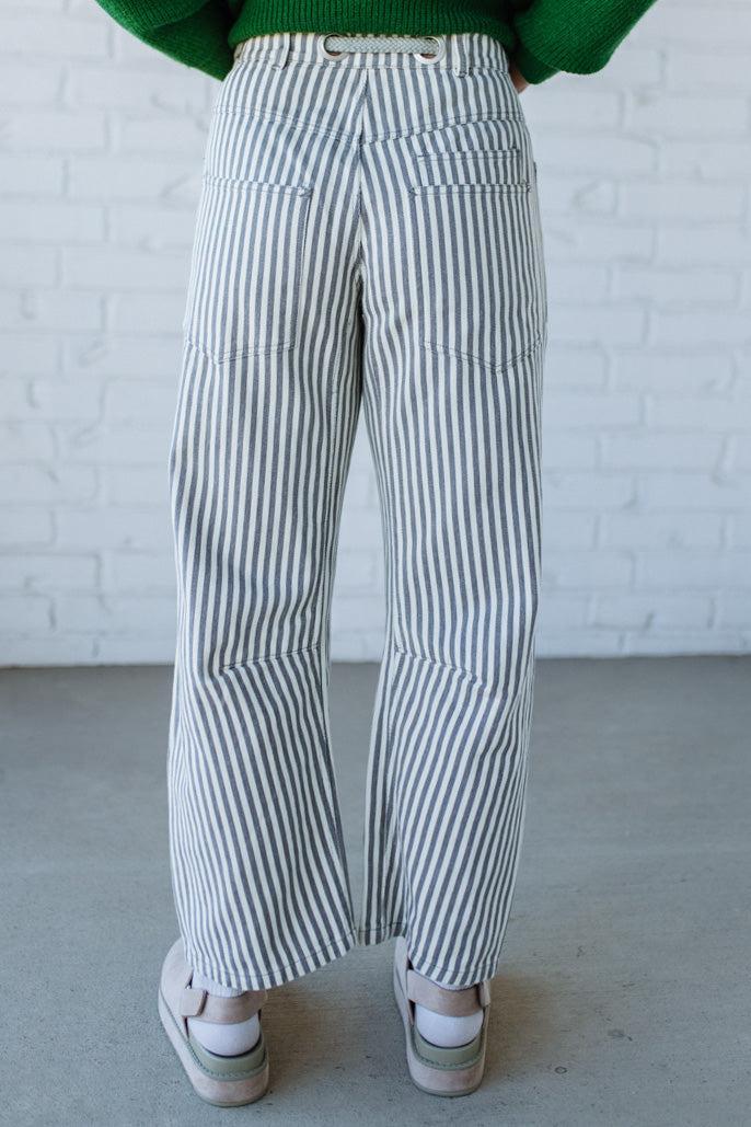 Woman wearing grey and cream vertical stiriped barrel cut jeans with a drawstring waist.
