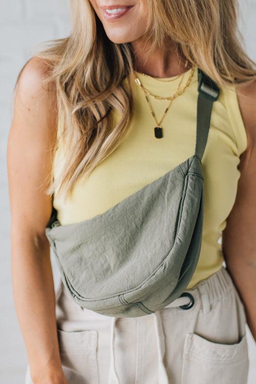 Blonde woman in a yellow tank wearing an olive green nylon slingbag.