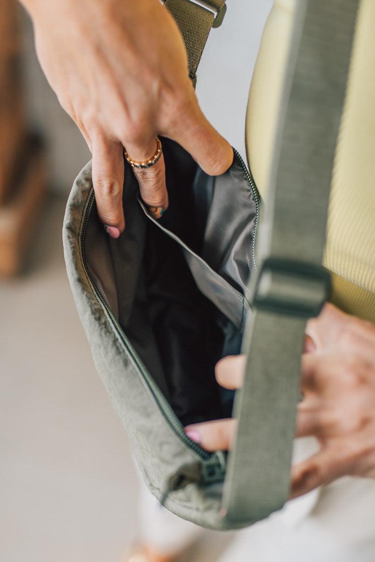 Blonde woman in a yellow tank wearing an olive green nylon slingbag.