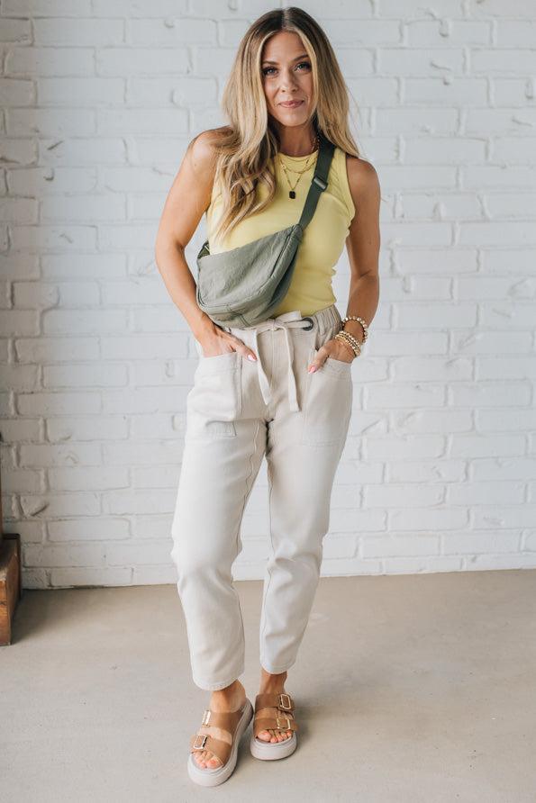 Blonde woman in a yellow tank wearing an olive green nylon slingbag.