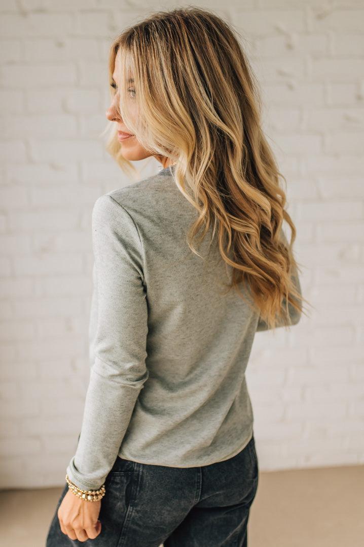 Woman wearing a gray long-sleeve top and dark jeans against a light background