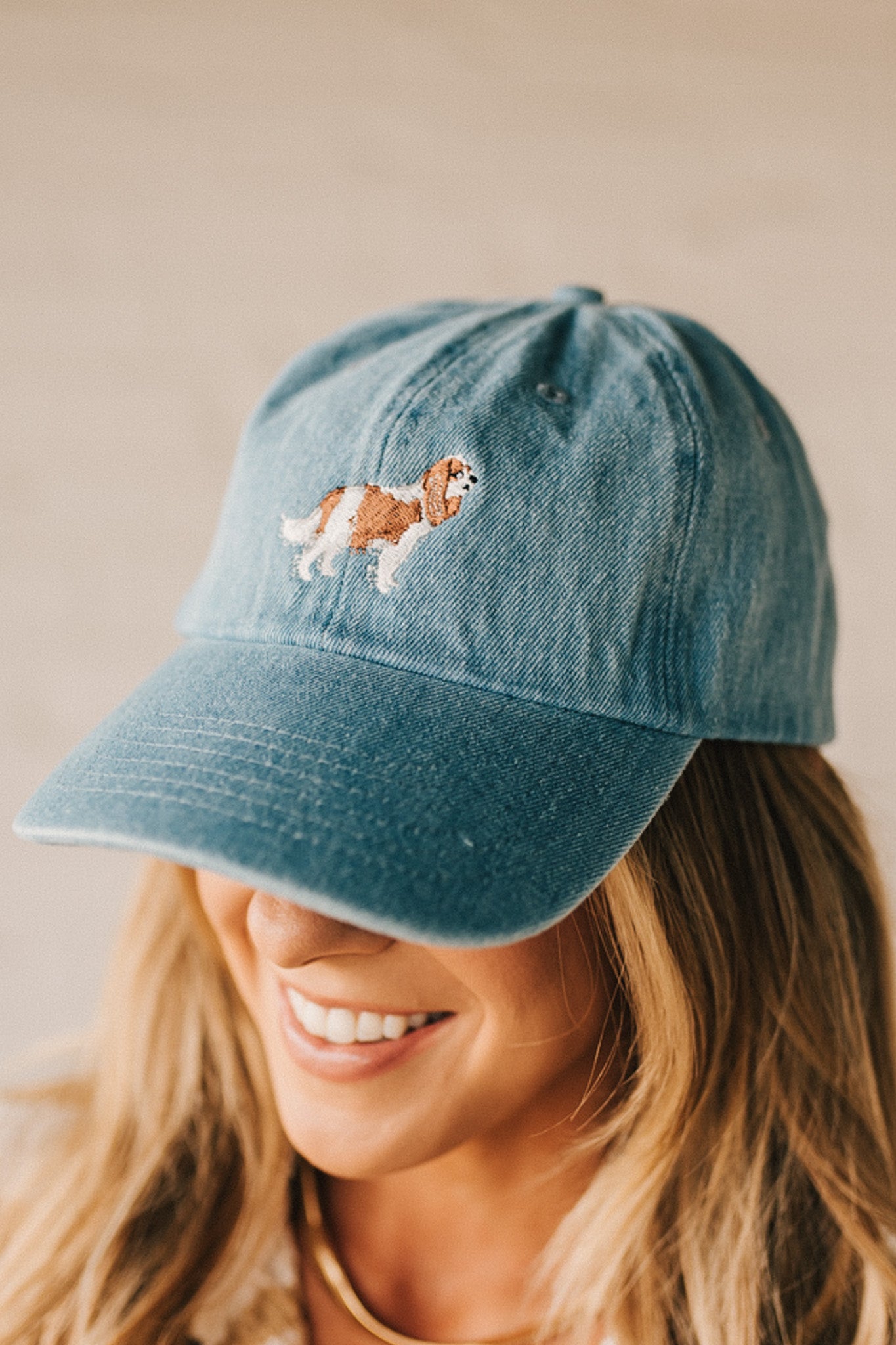 Blonde woman wearing a denim Hat with embroidered King Cavalier dog at front center.