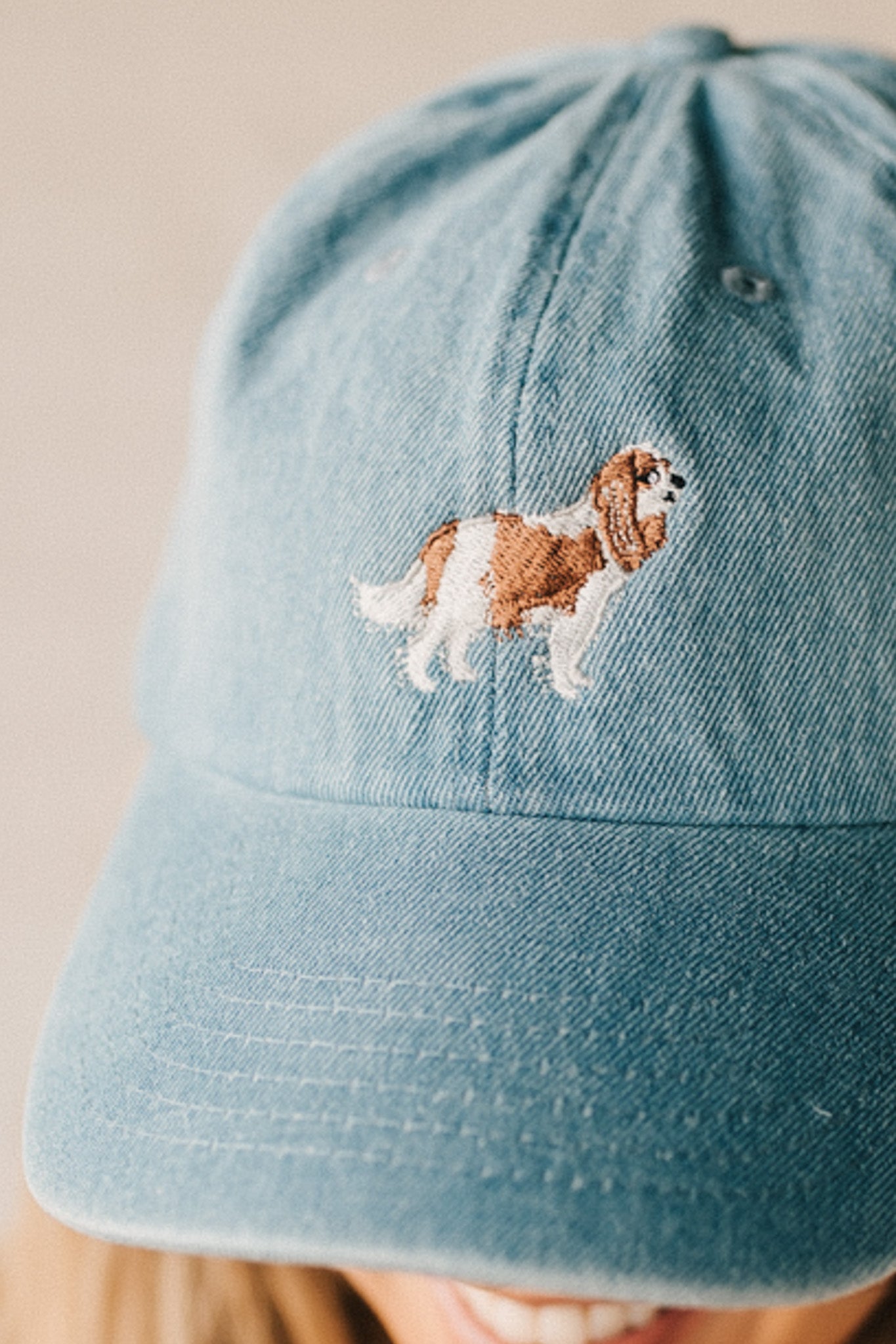Blonde woman wearing a denim Hat with embroidered King Cavalier dog at front center.