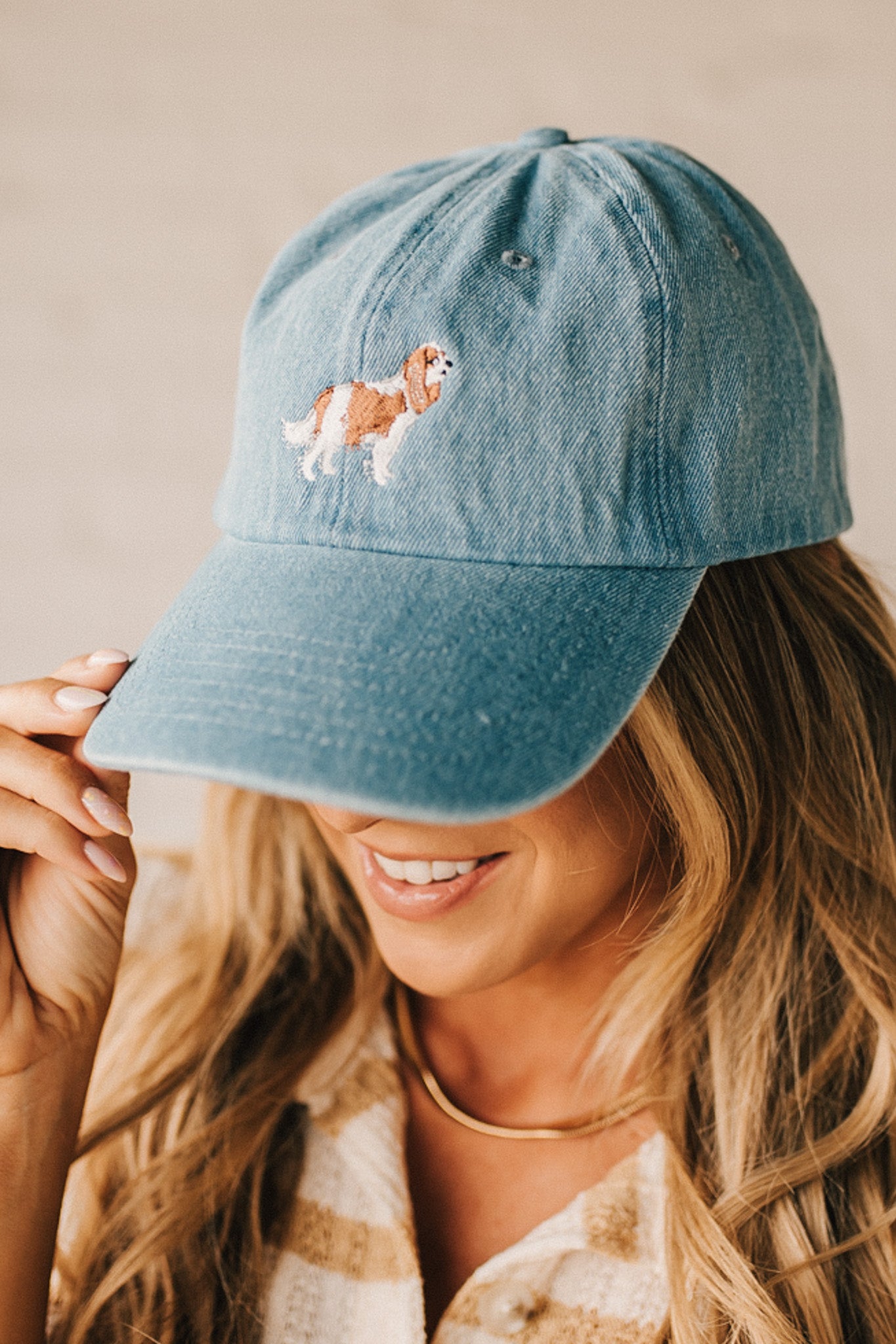 Blonde woman wearing a denim Hat with embroidered King Cavalier dog at front center.