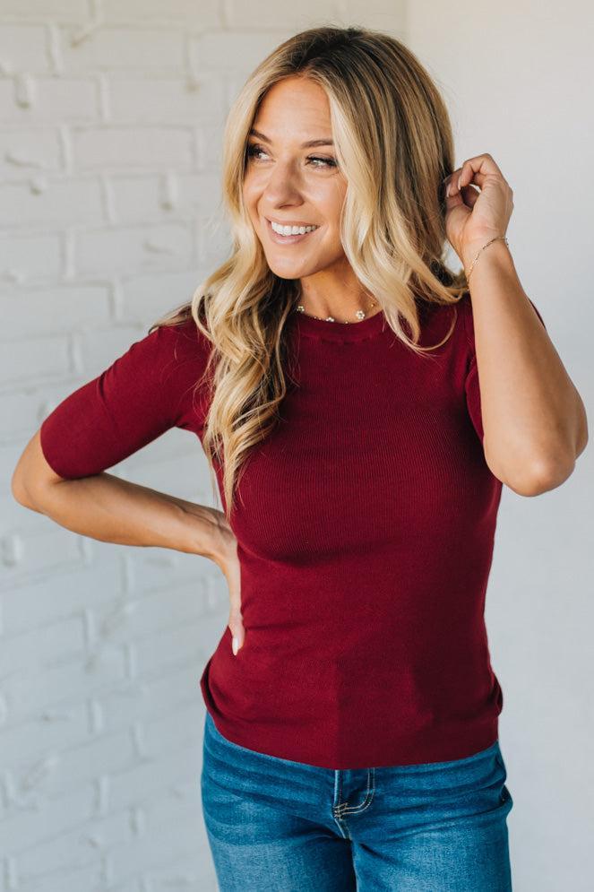Woman wearing a red top and blue jeans against a white brick wall