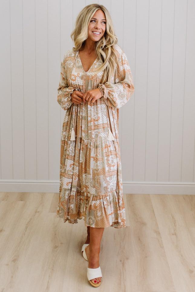 Woman wearing a floral dress standing against a white paneled wall.