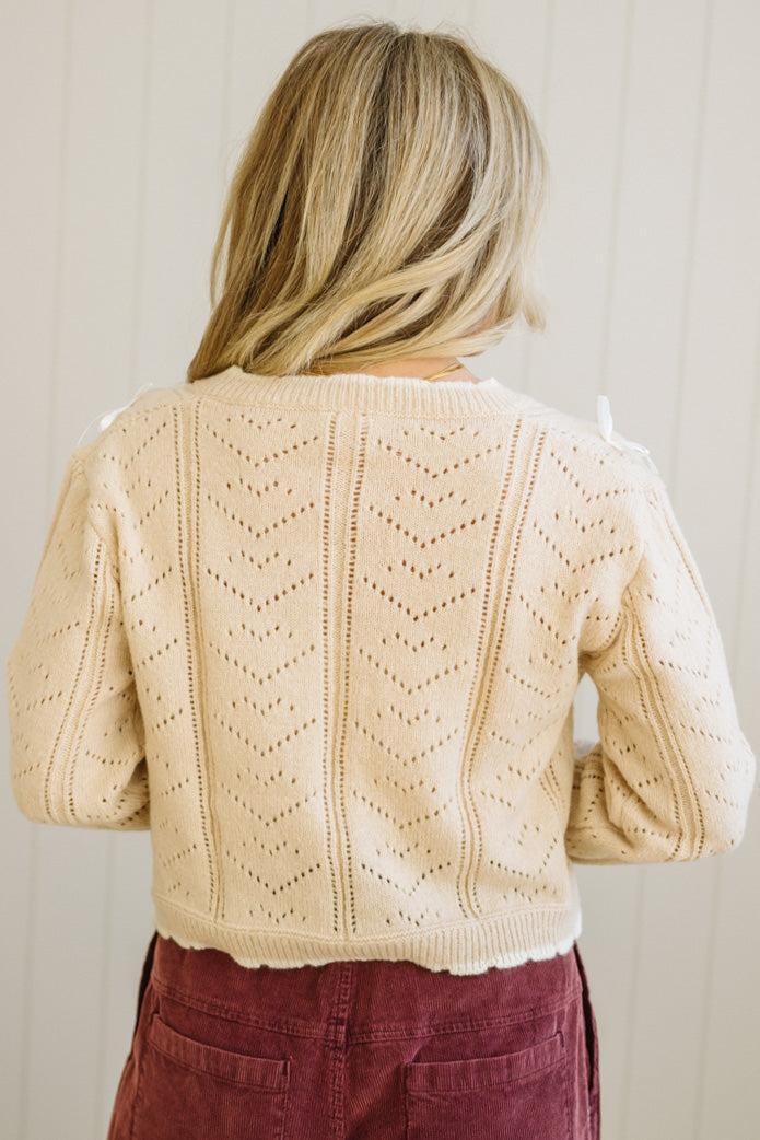 Person wearing a beige knitted cardigan with a subtle pattern against a plain background
