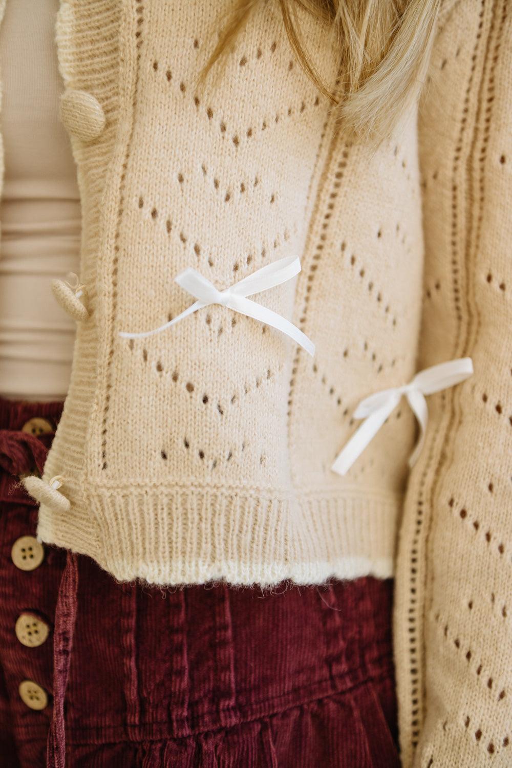 Close-up of a beige knitted vest with white accents worn over a red garment.