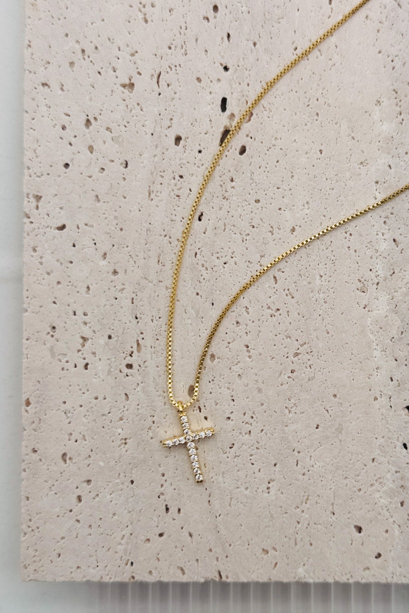 Gold necklace with a cross pendant on a textured beige surface