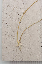 Gold necklace with a cross pendant on a textured beige surface