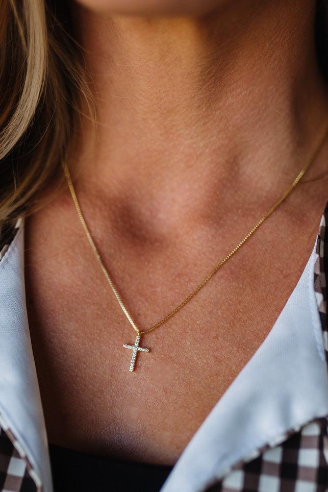 Close-up of a person wearing a gold necklace with a cross pendant.